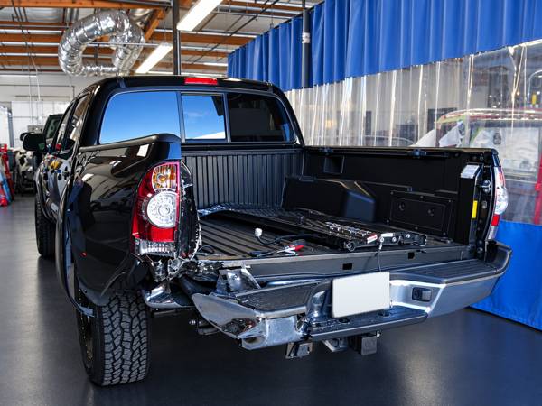 Black Toyota Tacoma with rear bumper damage in the shop