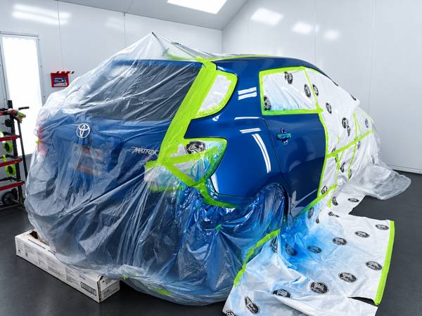 Blue hatchback masked with plastic and green tape for paint