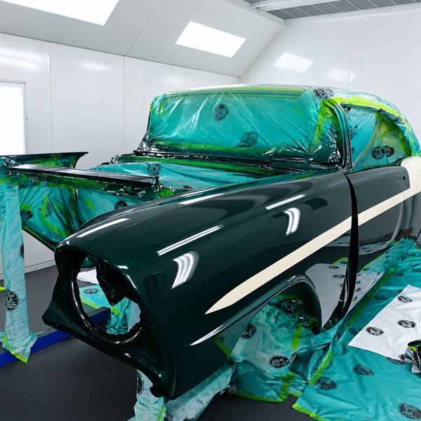 Dark green fender masked with fine-line tape in the paint booth