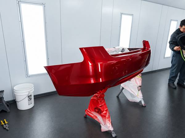 Red bumper cover drying on a stand in the paint booth