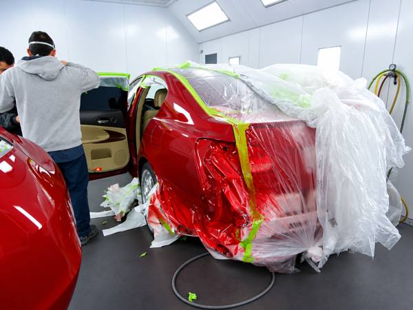 Red car masked for paint with a technician at work