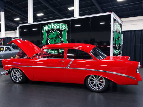 Red classic Chevy with the hood up beside the Mahood's trailer at a car show