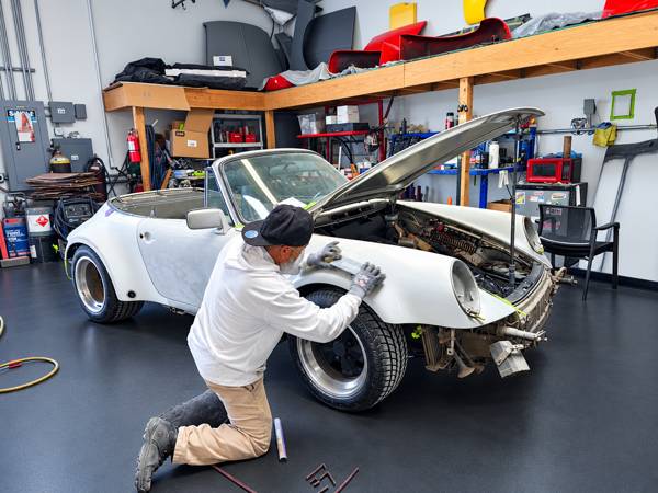 Technician working on the front fender of a white Porsche in the shop